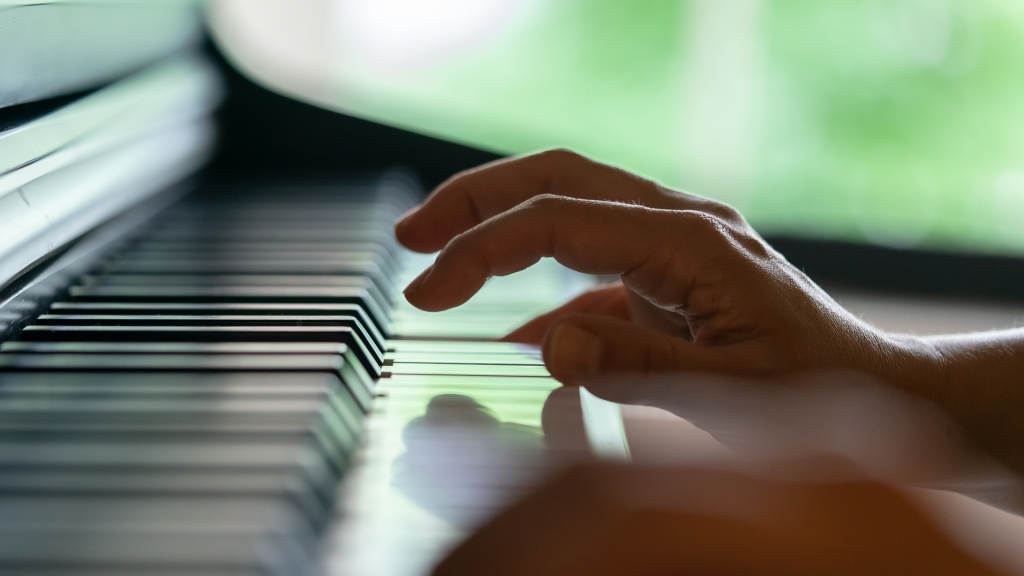closeup of hand playing keys on a piano with a blurred green background